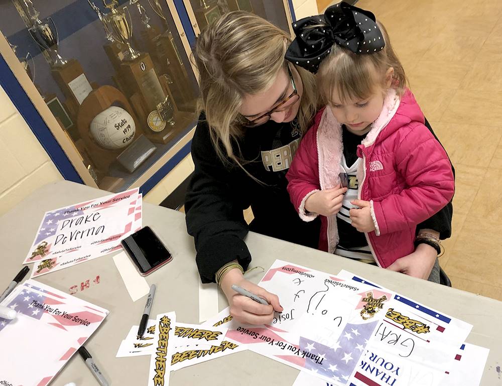 parent and young student signing a poster in gratitude for service