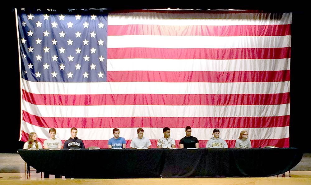 Students on stage in front of a large flag for signing day