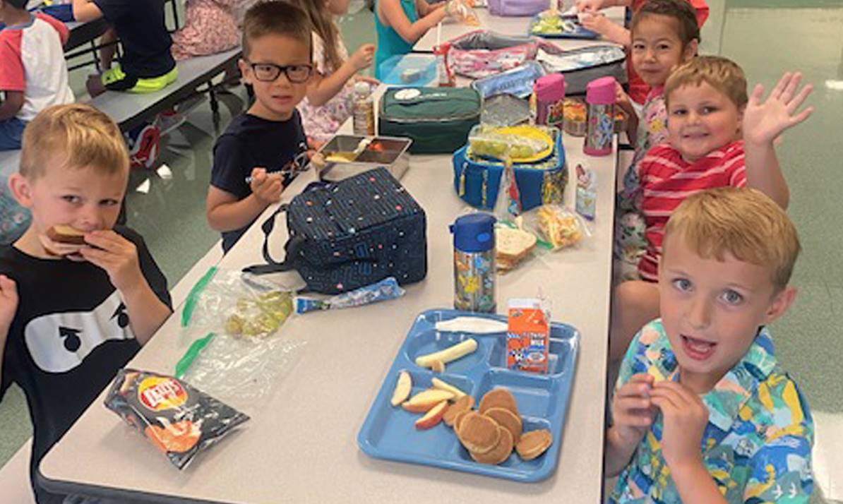 five students around cafeteria table waving