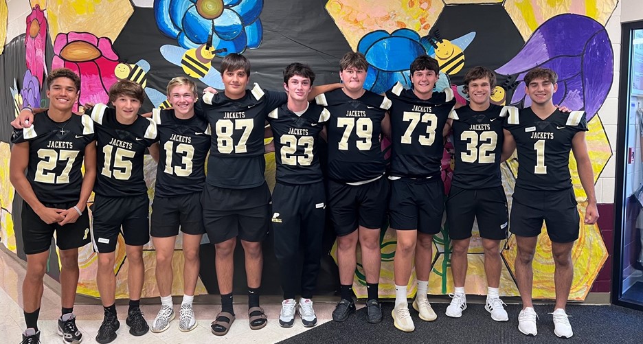 group of young men in football uniforms posing in front of a brightly colored mural