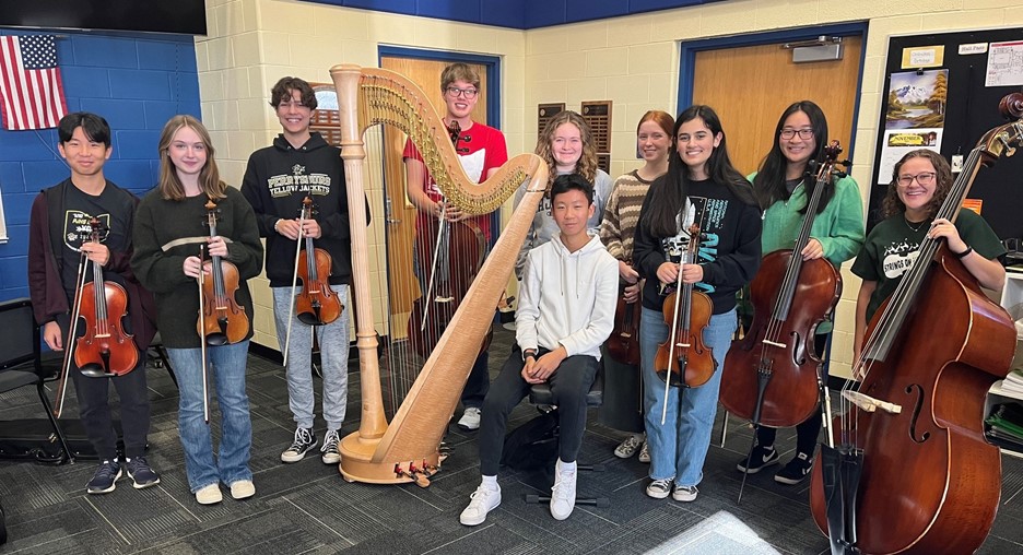 Orchestra students posing with instruments in classroom