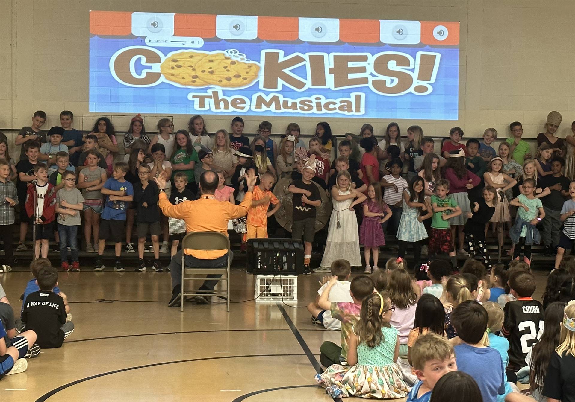 large group of students in risers with "Cookies! The Musical" projected on the wall