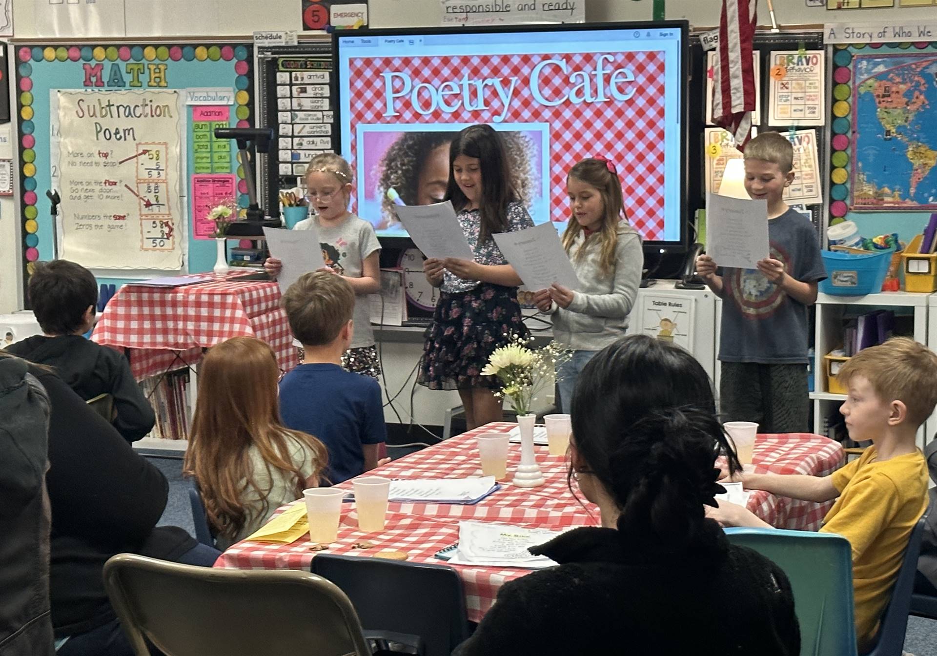 four students reading in front of class with "Poetry Cafe" projected on the screen